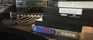 A stack of VHS tapes beside a VHS tape player ready to be transferred to DVD or Computer file
